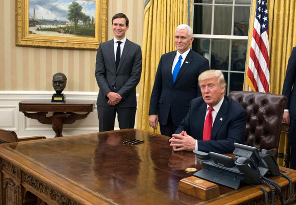 도널드 트럼프 대통령이 집무실 책상에  앉아 있고 그 옆에 마이크 펜스 부통령과 큰 사위 재러드 쿠슈너가 지켜보고 있다. 사진 왼쪽 중앙에 새로 진열된 처칠 두상이 보인다. (사진=EPA)