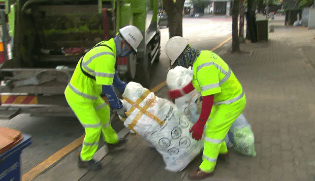 환경미화원들이 '쓰레기 혹'이 달린 봉투를 청소차로 옮기고 있다.