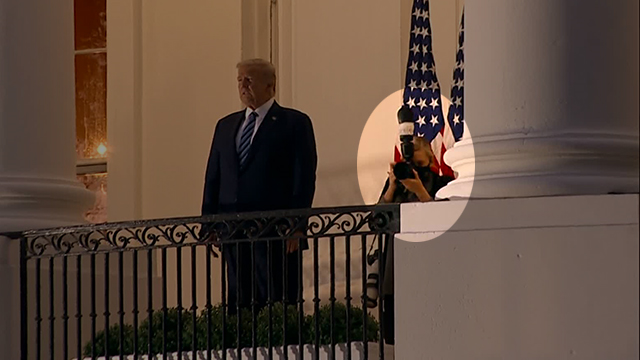 백악관 2층 난간에서 마스크를 벗고 서 있는 트럼프 대통령. 그 오른쪽 뒤쪽으로 이를 촬영하고 있는 사진사가 보인다.