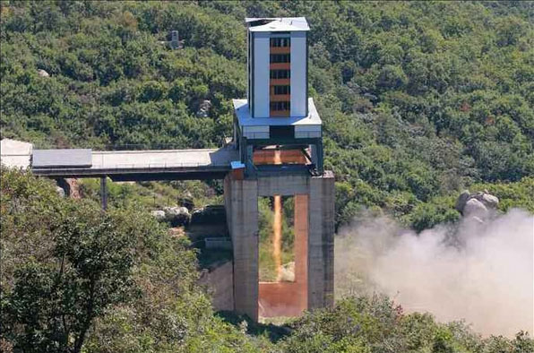 미사일 발사대로 추정되는 장치에 로켓 엔진이 설치돼있고, 긴 불꽃이 아래로 뿜어져 나오고 있다. 북한은 이번 로켓 엔진 실험이 성공적으로 진행됐다고 주장했다. (출처: 노동신문)