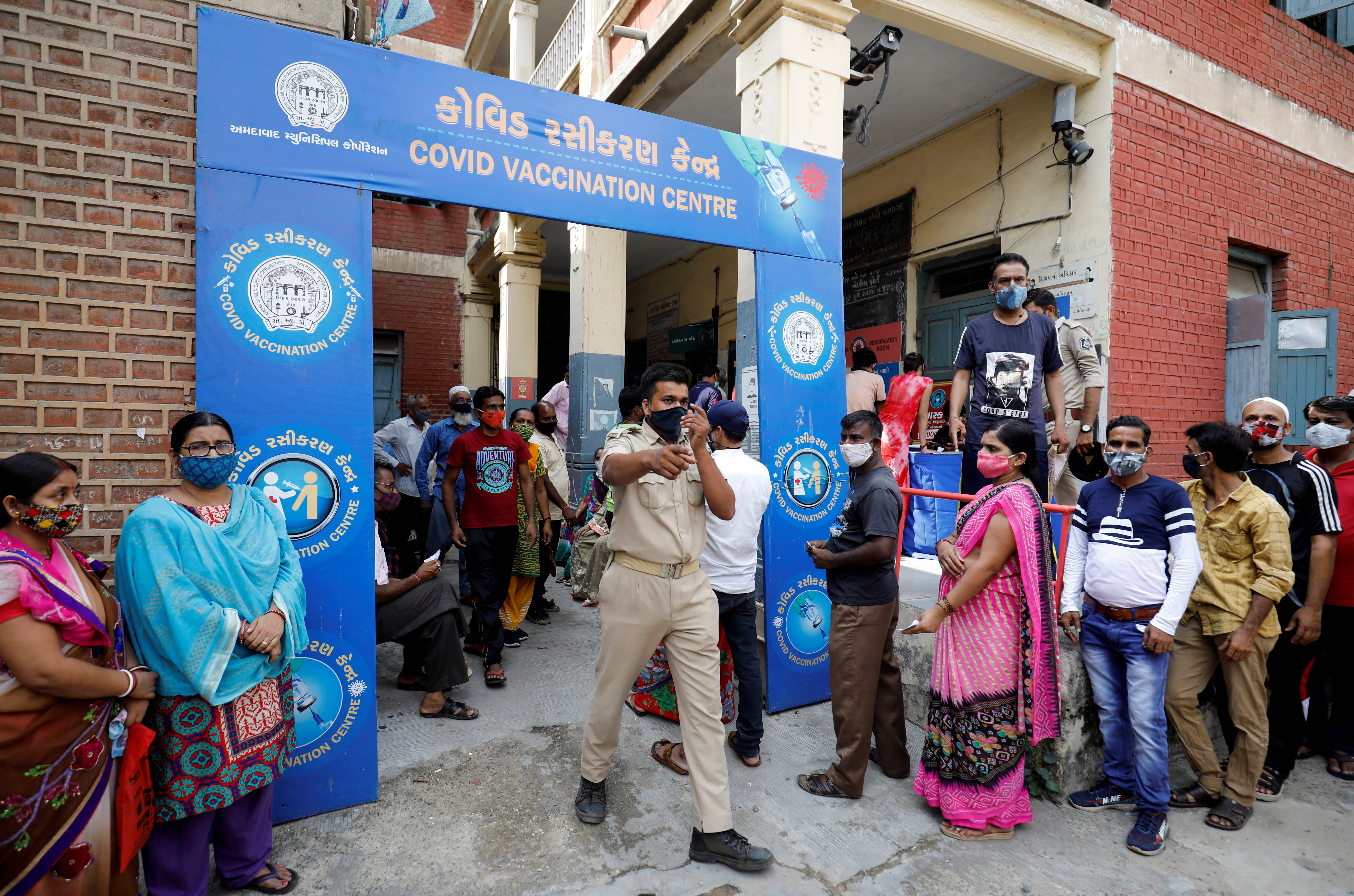 6월 30일 인도 구자라트주 아마다바드에서 한 경찰관이 코로나 바이러스 백신 접종을 받기 위해 줄 서고 있는 사람들을 정리하고 있다. [사진 출처 : 로이터=연합뉴스]