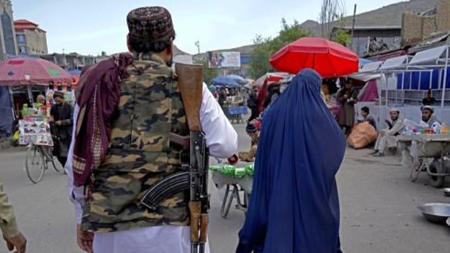 아프가니스탄 카불에서 탈레반 대원 옆에서 한 여성이 부르카를 입고 걷는 모습