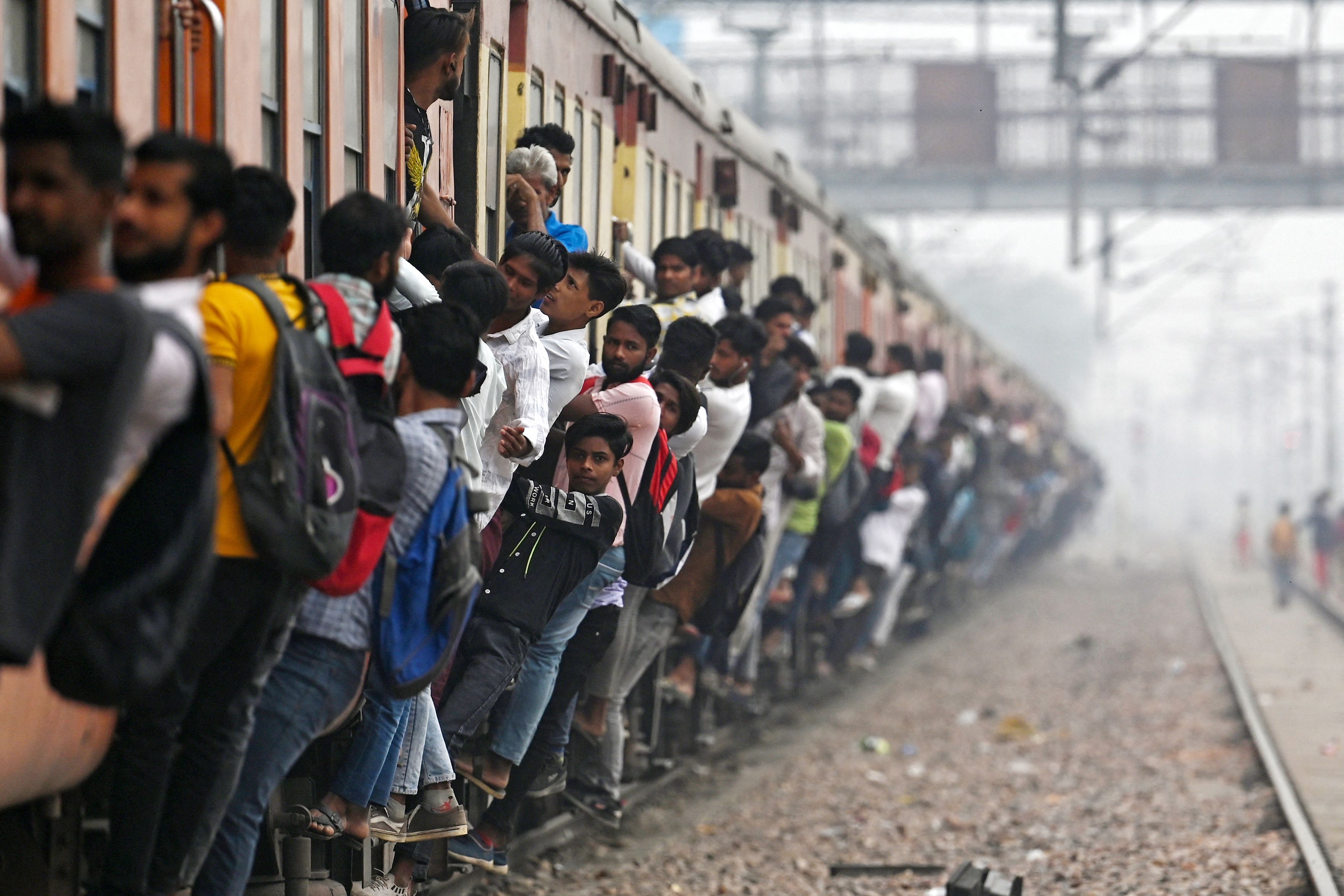 인도 우타르 프라데시 주의 기차역 출근길. 사람들이 만원 열차에 매달려 있다. (AFP)