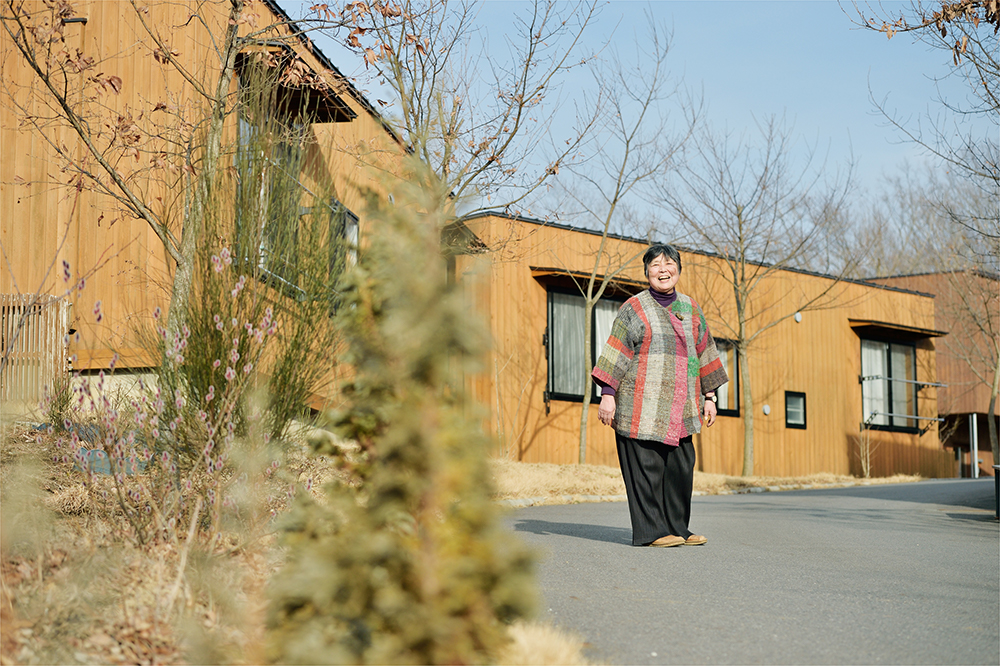 60대의 치카야마 씨가 자신이 기획한 한 노인 주택 앞에서 포즈를 취하고 있다. 