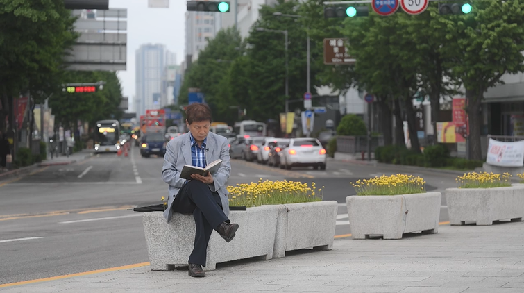 유영옥 씨가 5·18의 상징적 장소인 광주 금남로를 등지고 앉아 자신의 일기장을 읽어보고 있다.